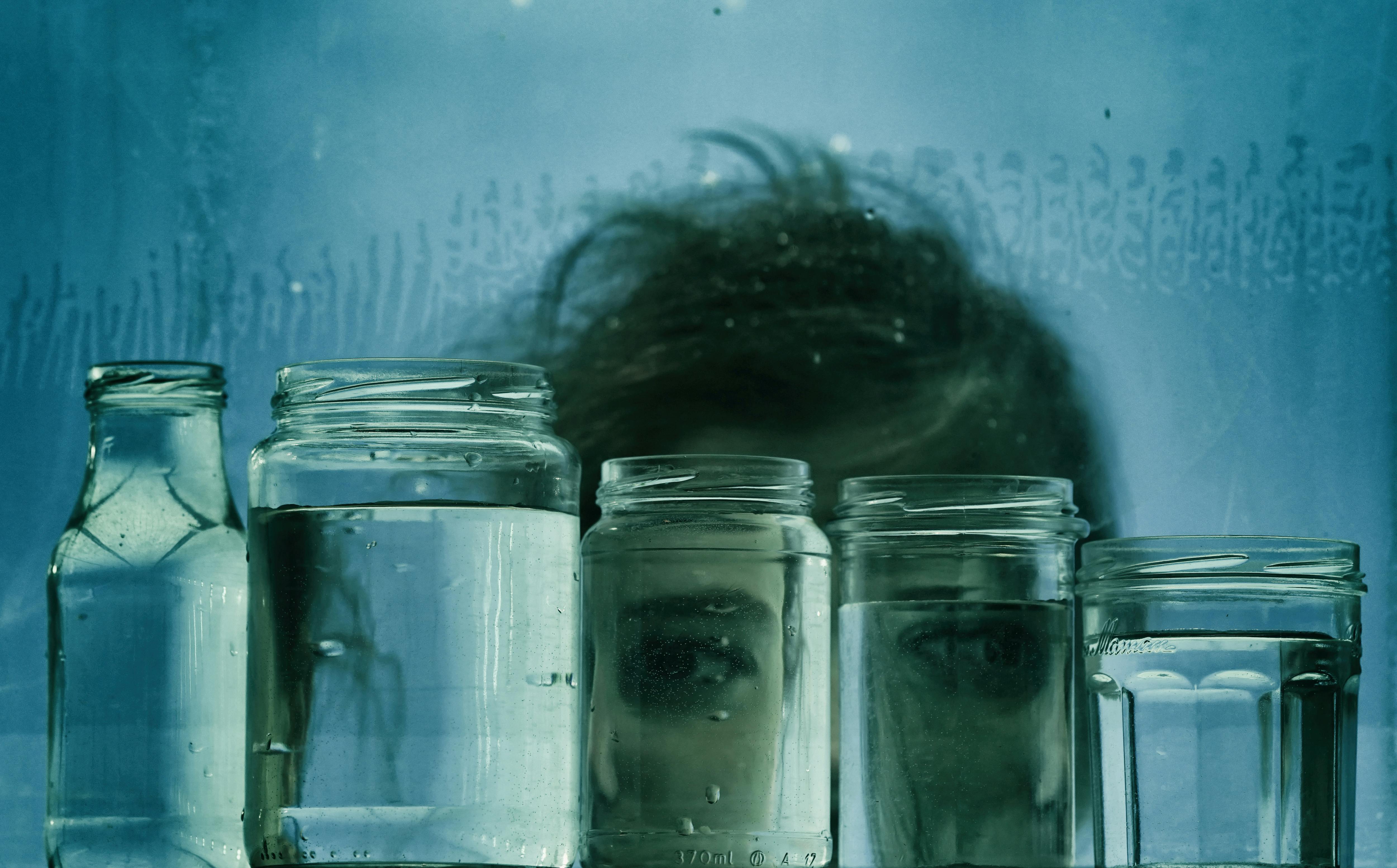 Artistic image of a face distorted through multiple water-filled jars, creating a creative and surreal visual effect.