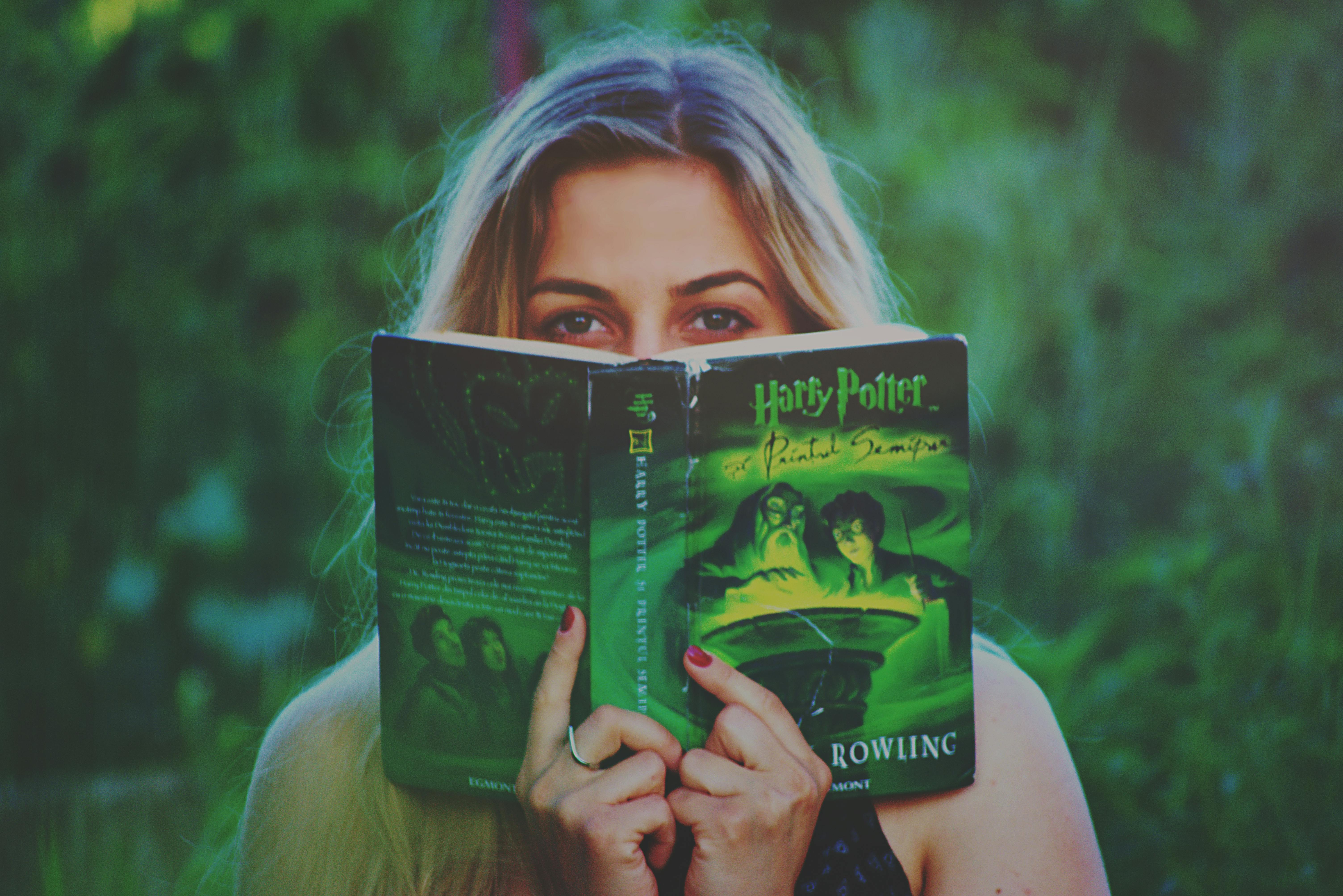 A woman reading a Harry Potter book amidst greenery, enjoying leisure time.